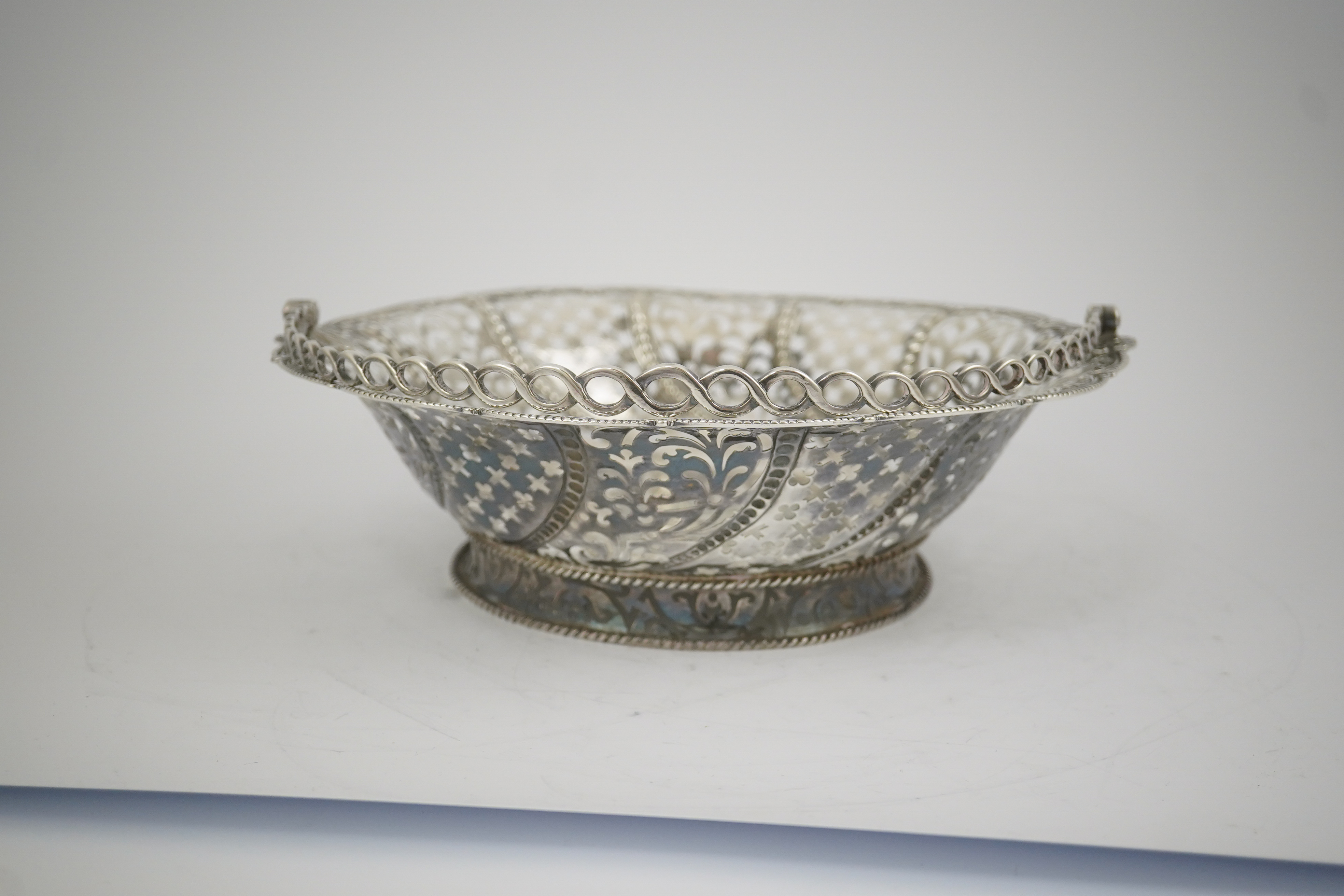 A late George II pierced silver cake basket, by William Plummer?, of shaped circular form, with engraved crest and multi ring handle, London, 1759, diameter 29.2cm, 25.5oz. (a.f.). Condition - poor